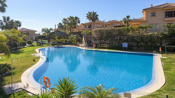 A swimming pool with a curved edge, surrounded by a stone wall and palm trees. - Villa Riviera in Urbanizaci n Riviera Sol (Mijas)