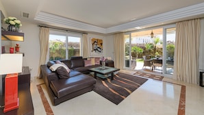 A modern living room with a leather sofa, a glass coffee table, and a view of the outdoors through large sliding glass doors. - Villa Riviera in Urbanizaci n Riviera Sol (Mijas)