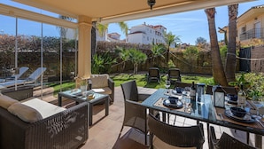 An outdoor patio with wicker furniture, a glass table, and a view of a white building in the background. - Villa Riviera in Urbanizaci n Riviera Sol (Mijas)