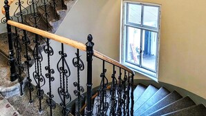 Eine geschwungene Treppe mit aufwendigen schwarzen Metallgeländern und Holzhandläufen, die zu einer Zwischenebene mit einem Fenster führt.