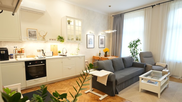 Ein modernes Wohnzimmer mit grauem Sofa, einem Couchtisch und einem Essbereich mit Tisch und Stühlen.