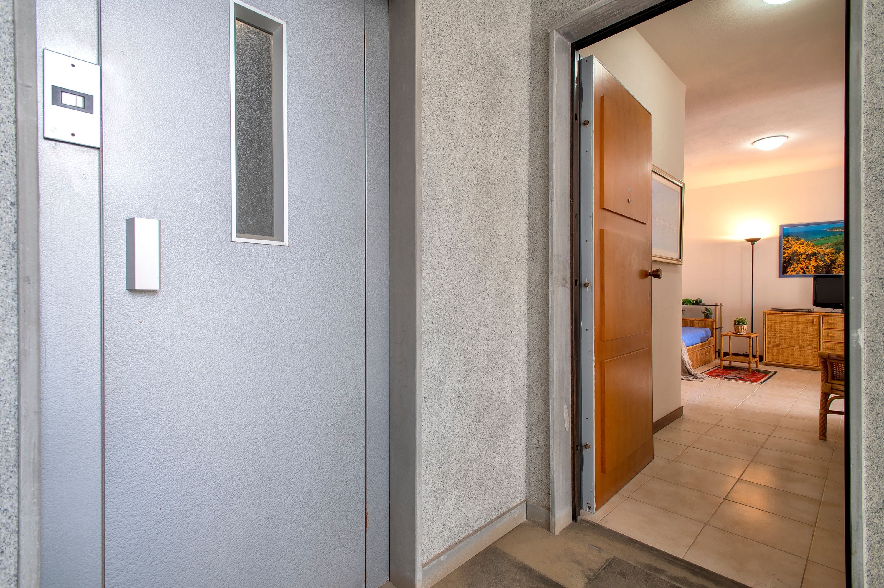 A hallway leading to a room with a bed, a small table, a lamp, and a painting on the wall.