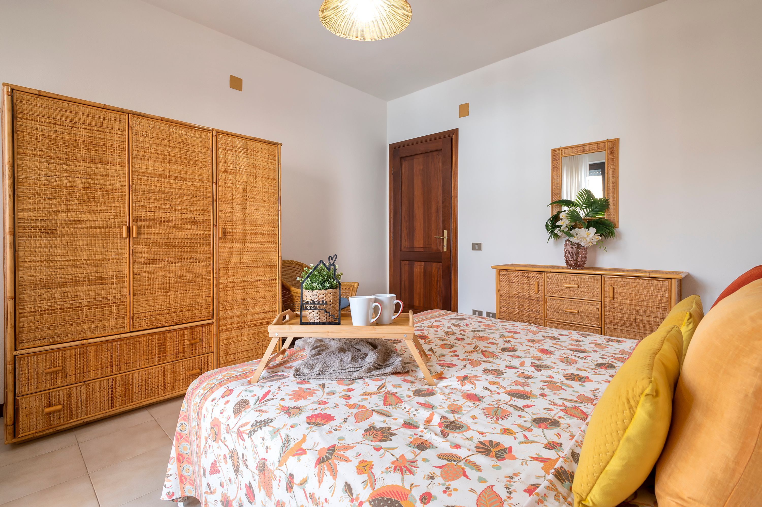 A bedroom with a bed, a wardrobe, a bedside table with a plant, a mirror, and a door.