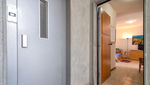 A hallway leading to a room with a bed, a small table, a lamp, and a painting on the wall. - Sardinia RE - Lilium Central Flat (Alghero)