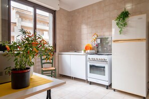 Cocina compacta con estufa, horno y refrigerador. Una ventana ofrece vistas al exterior.