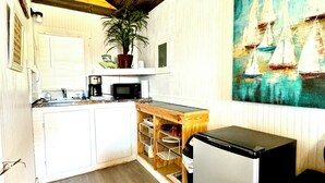 A compact kitchen with wooden cabinets, a microwave, a sink, and a refrigerator. There's a potted plant on the counter and a painting of sailboats on the wall.