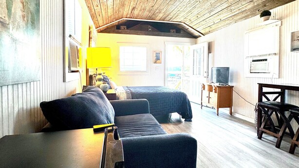 A room with a wooden ceiling, a bed, a desk, and a chair.