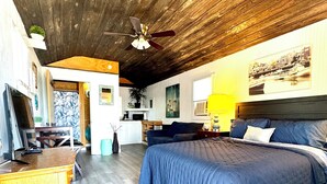 A bedroom with a large bed, wooden ceiling, and a television on a wooden dresser.