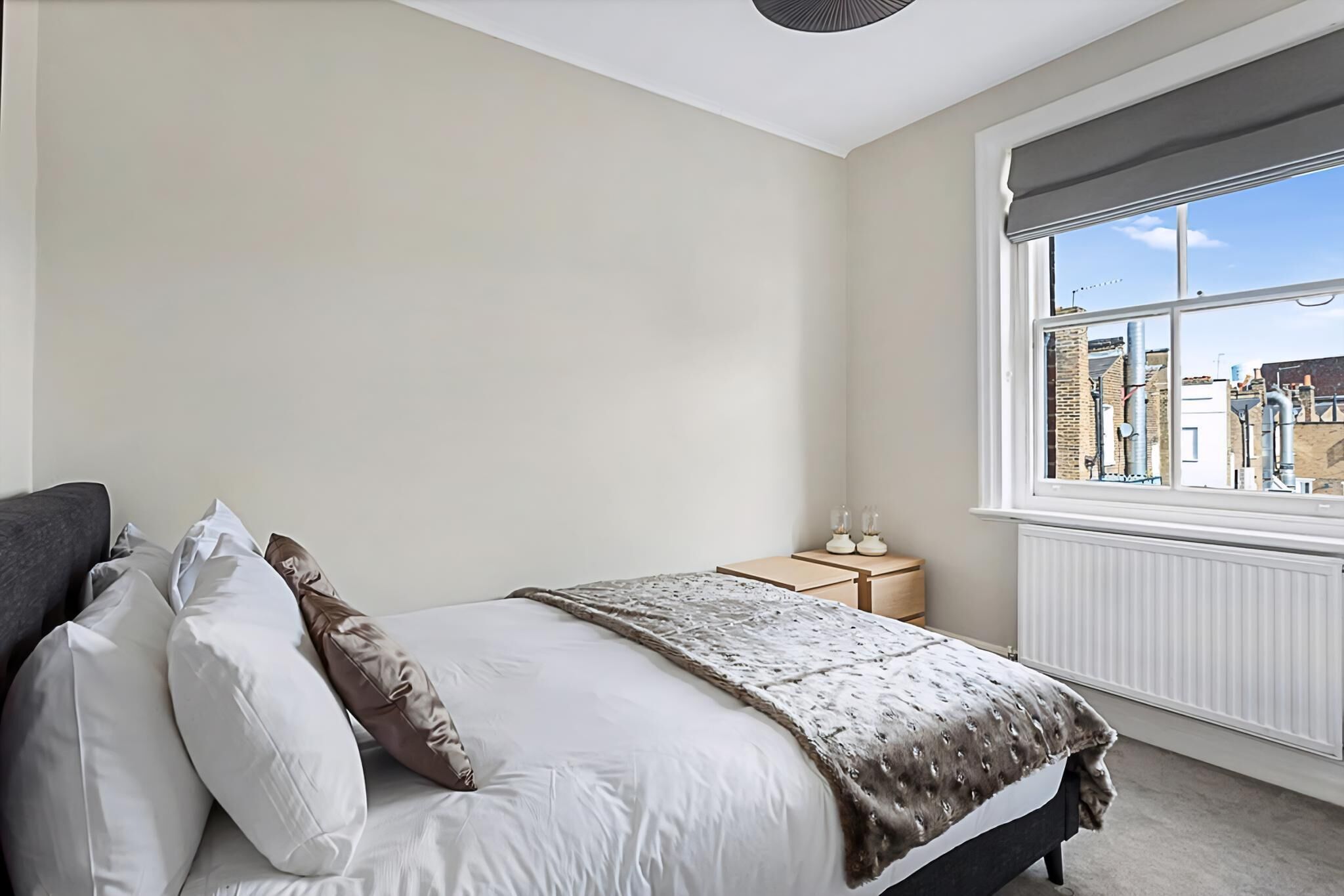 A bedroom with a bed, pillows, a bedside table with glasses, and a window with a view of buildings.