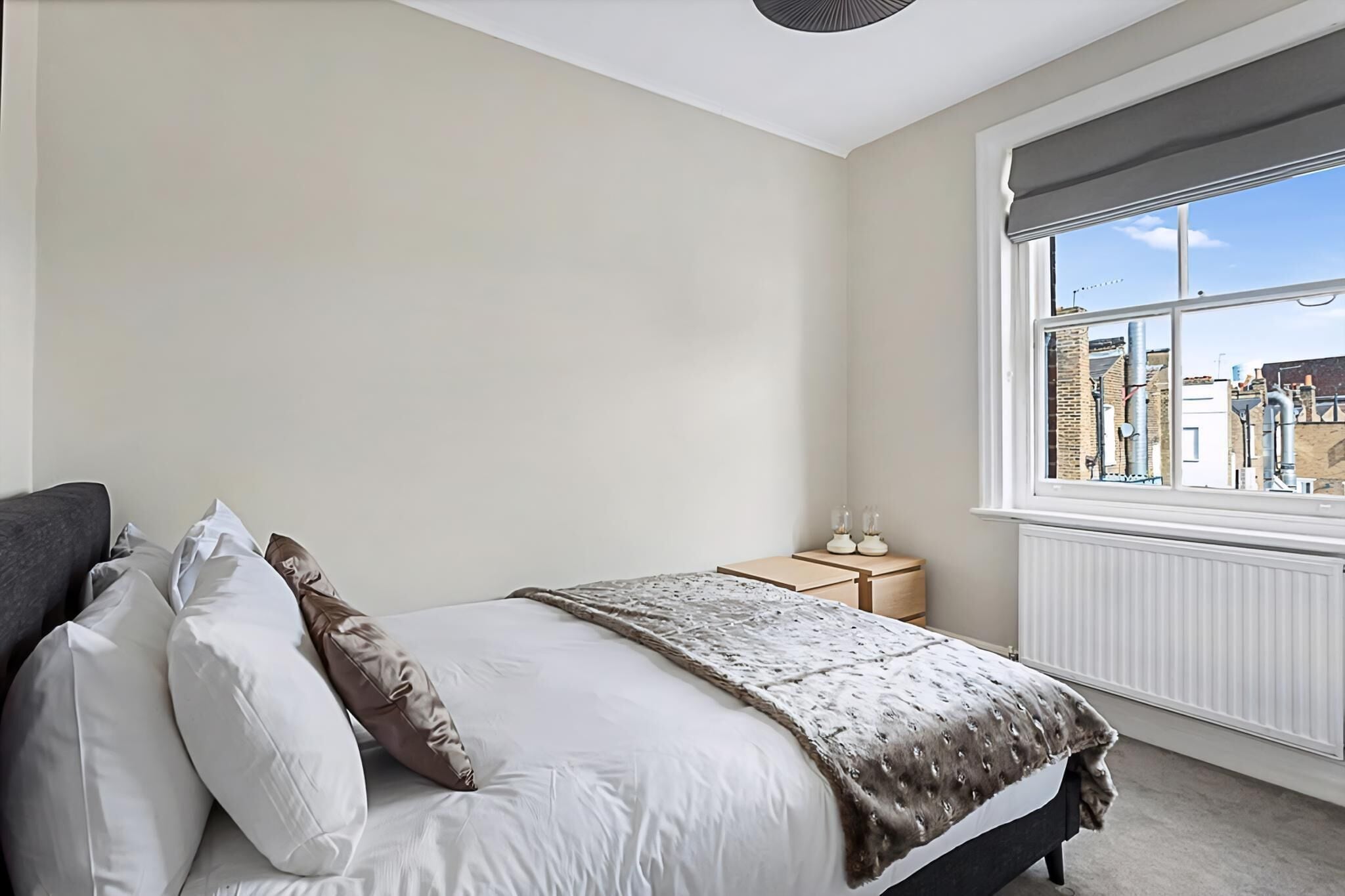 A bedroom with a bed, pillows, a nightstand, and a window with a view of buildings.