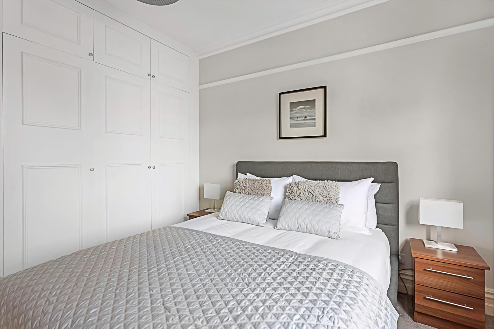 A neatly arranged bedroom with a bed, bedside tables, and a wardrobe.