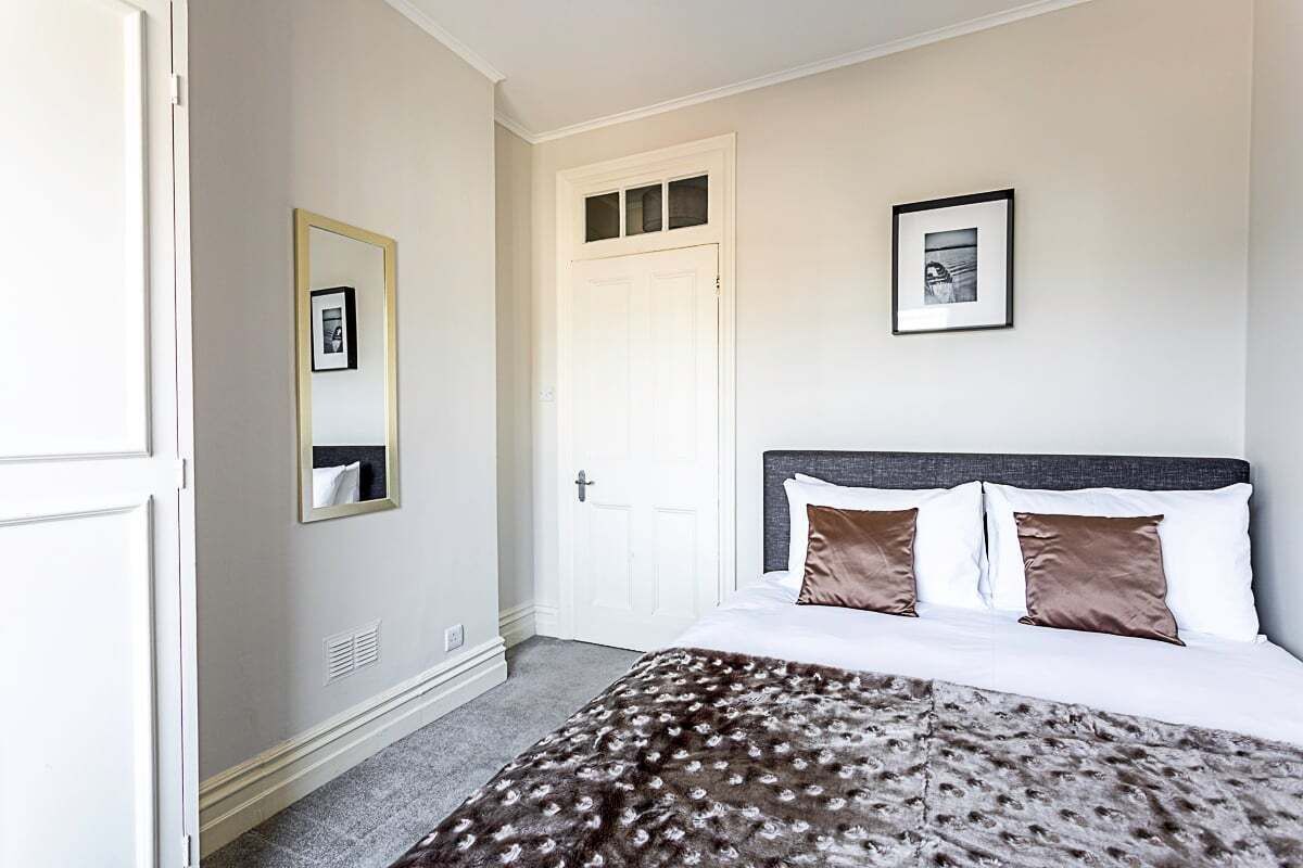 A bedroom with a bed, a door, a mirror, and a framed picture on the wall.