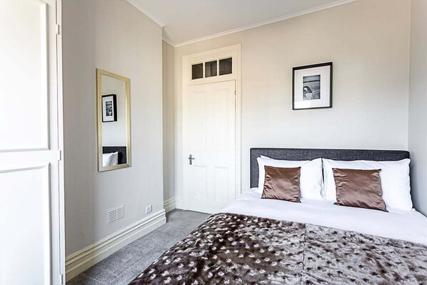 A bedroom with a bed, a door, a mirror, and a framed picture on the wall. - Serene 2BR - 3 Mins to Fulham Broadway (London)