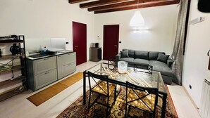 Ein modernes Wohnzimmer mit einer Couch, einem Esstisch mit Stühlen, einer Küchenzeile mit Schränken und einer Decke mit sichtbaren Holzbalken.