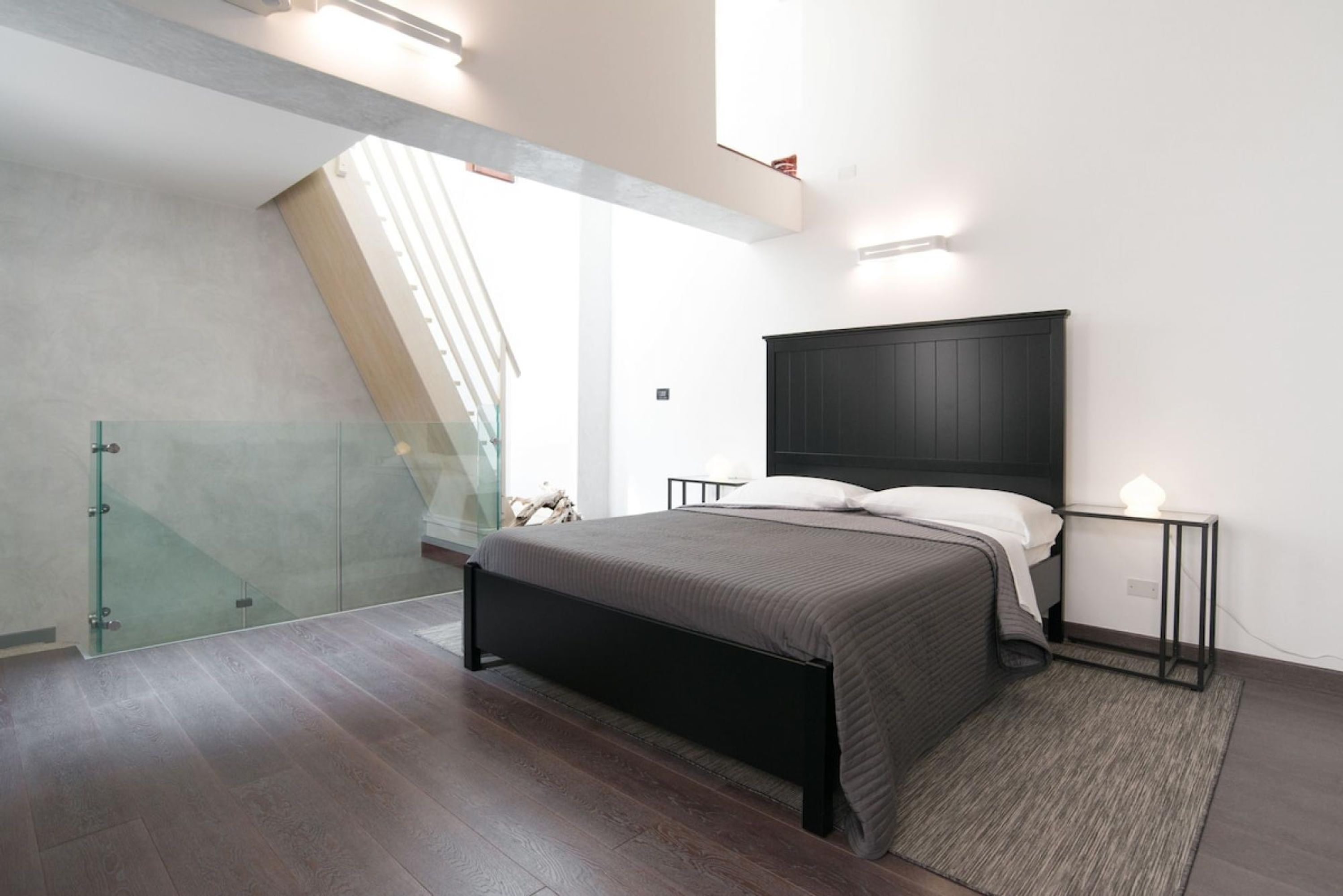 Quarto moderno com cama grande, parede de vidro e escada.