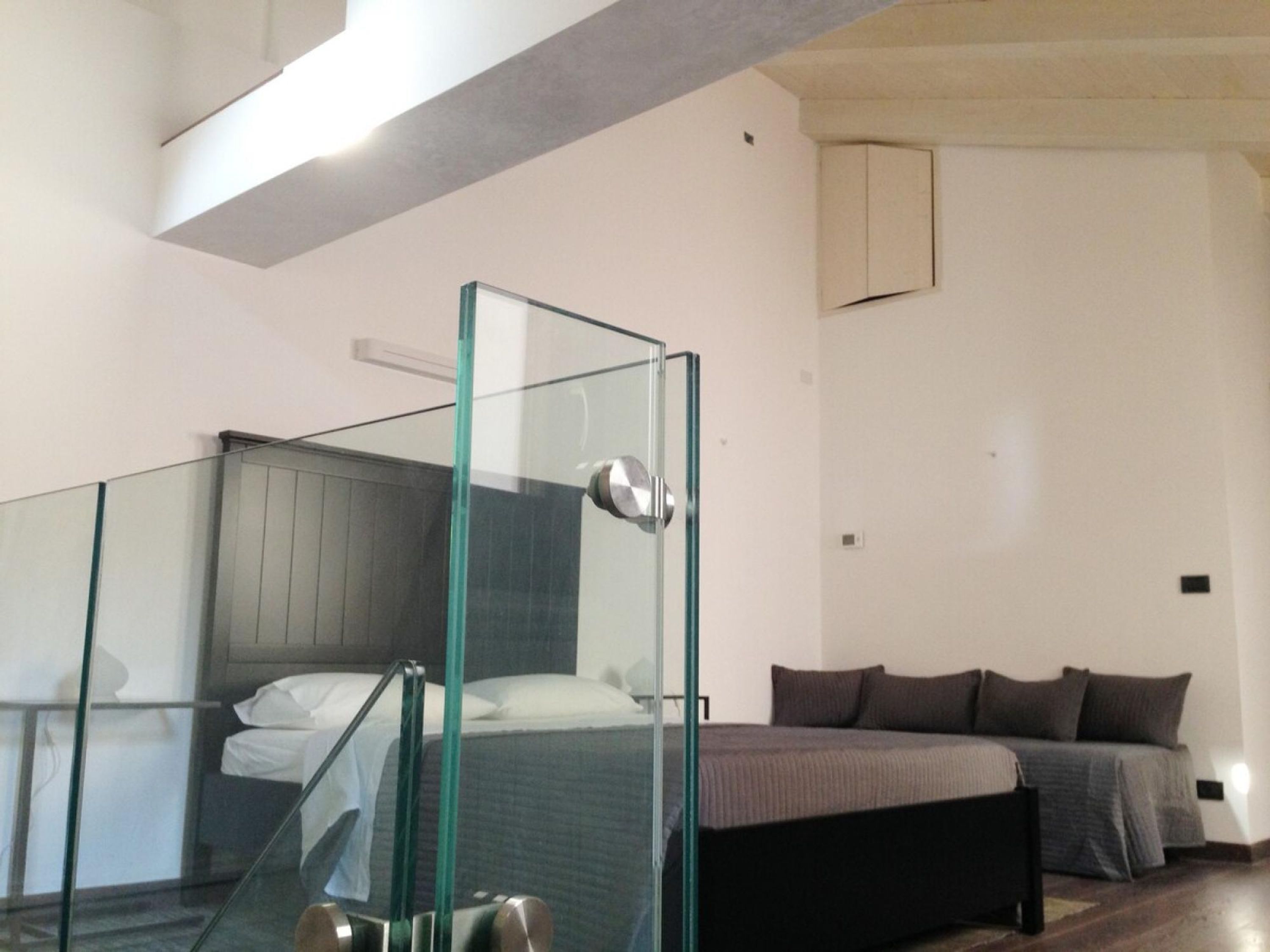 Una camera da letto moderna con cabina doccia in vetro, un letto con biancheria da letto scura e un armadio a vista.