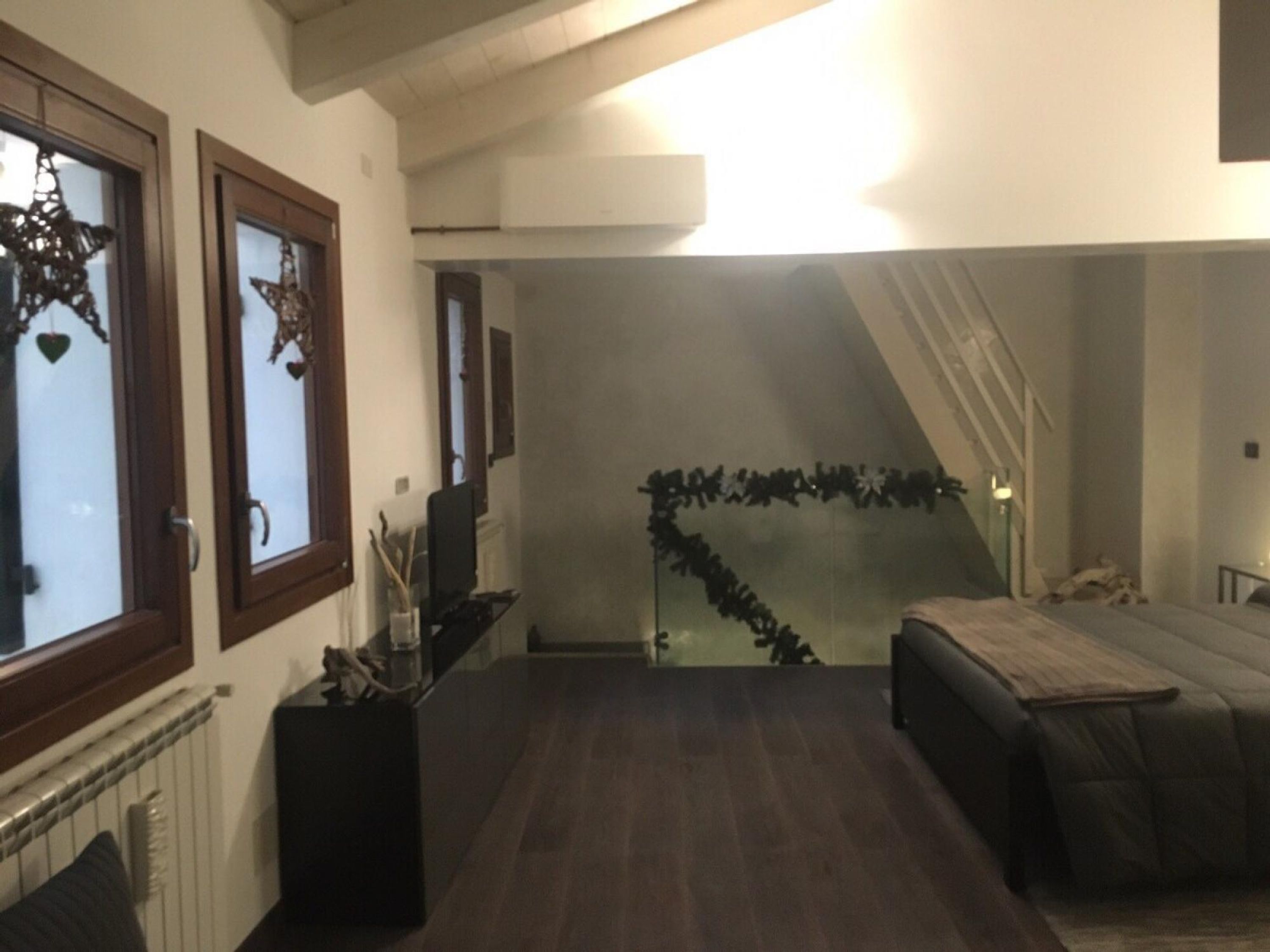A modern living room with a dark wood floor, a sofa, a coffee table, and a fireplace. There is a staircase leading to an upper level.