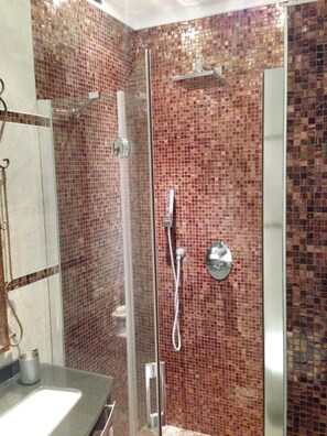 A glass-enclosed shower with a tiled wall, a chrome showerhead, and a handheld shower attachment. - Luxury S A San Marco Palace 3mins From San Marco (Venice)