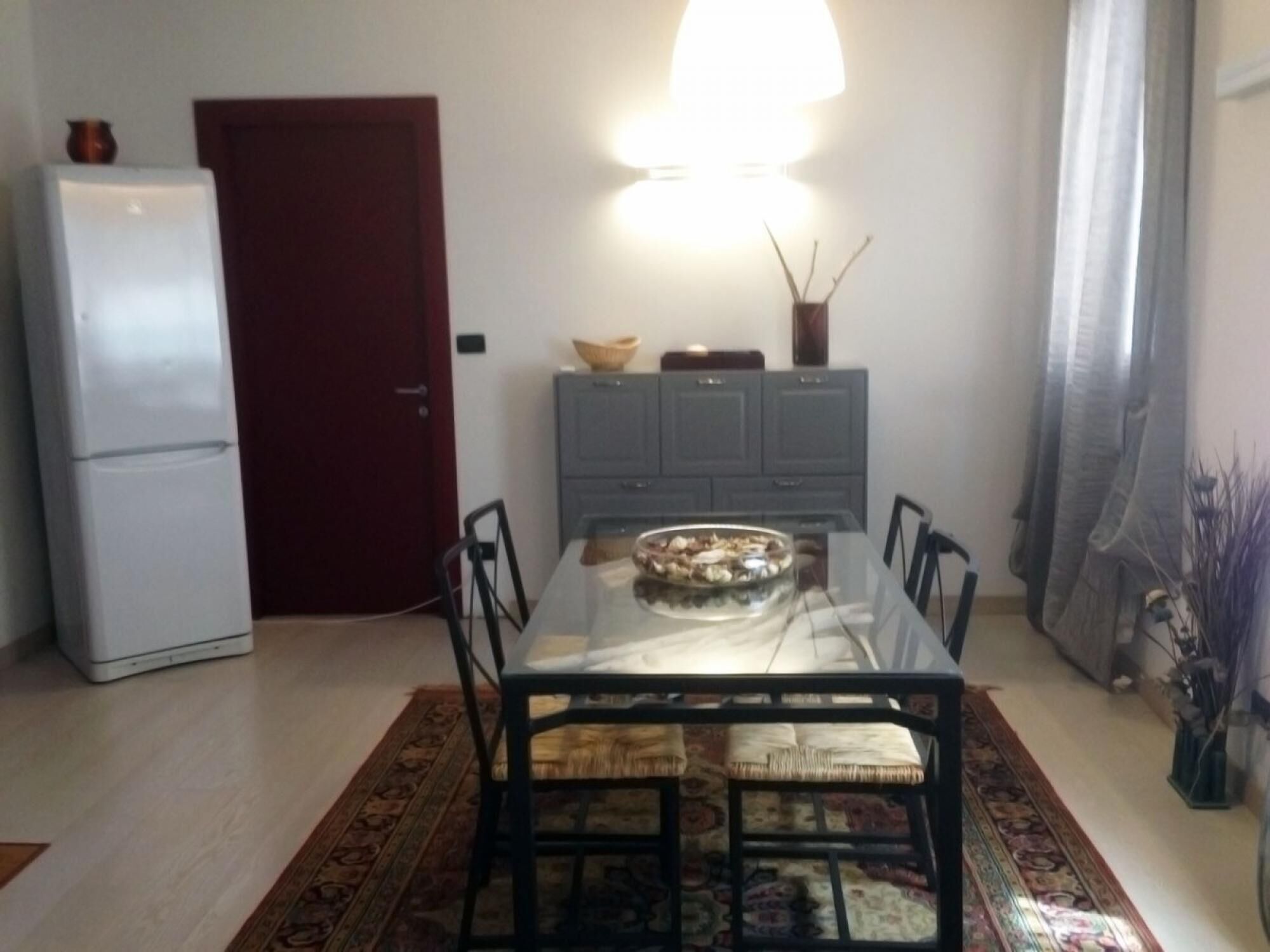 Um espaço de estar compacto com uma mesa de jantar rodeada por cadeiras, um frigorífico, um armário e uma tigela decorativa sobre a mesa.