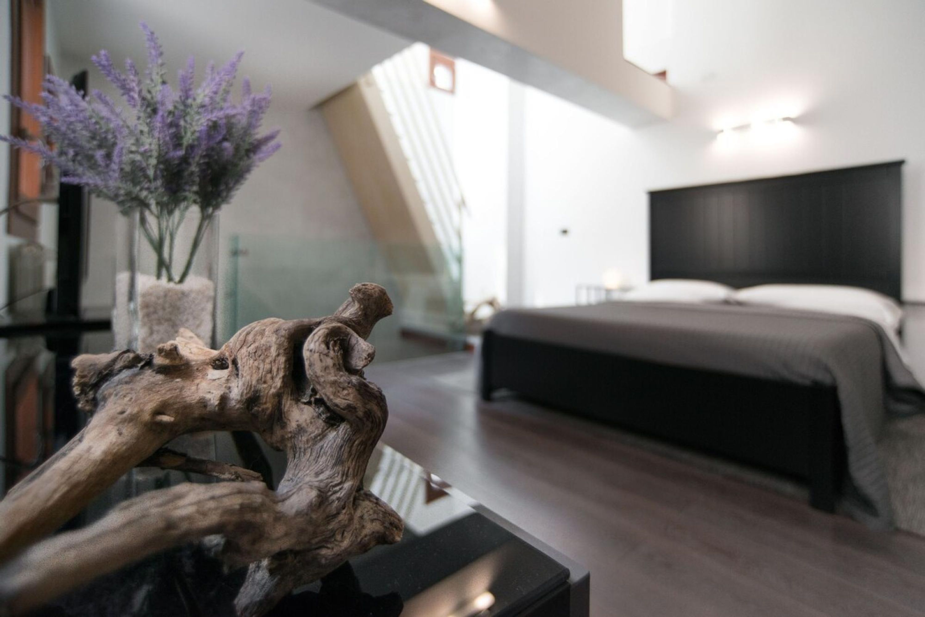 Een moderne slaapkamer met een groot bed, een houten sculptuur op een tafel en een bloemenvaas.