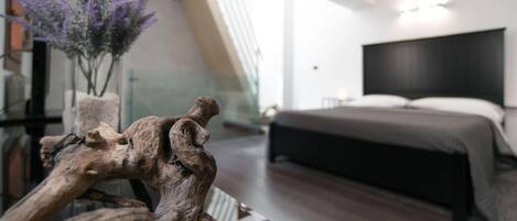 Een moderne slaapkamer met een groot bed, een houten sculptuur op een tafel en een bloemenvaas.