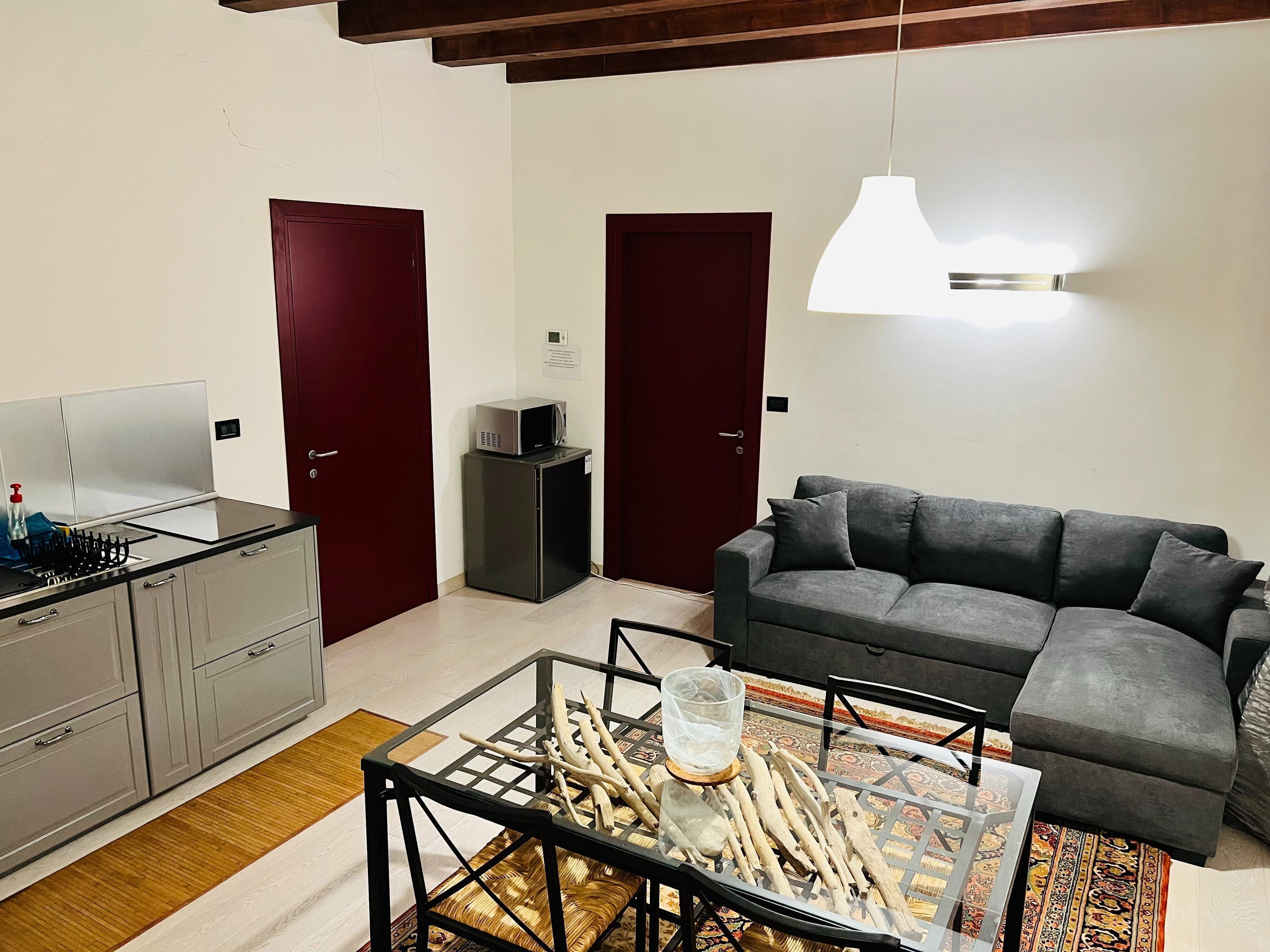 A compact living space with a kitchenette, a sofa, a glass coffee table, and a hanging light fixture.