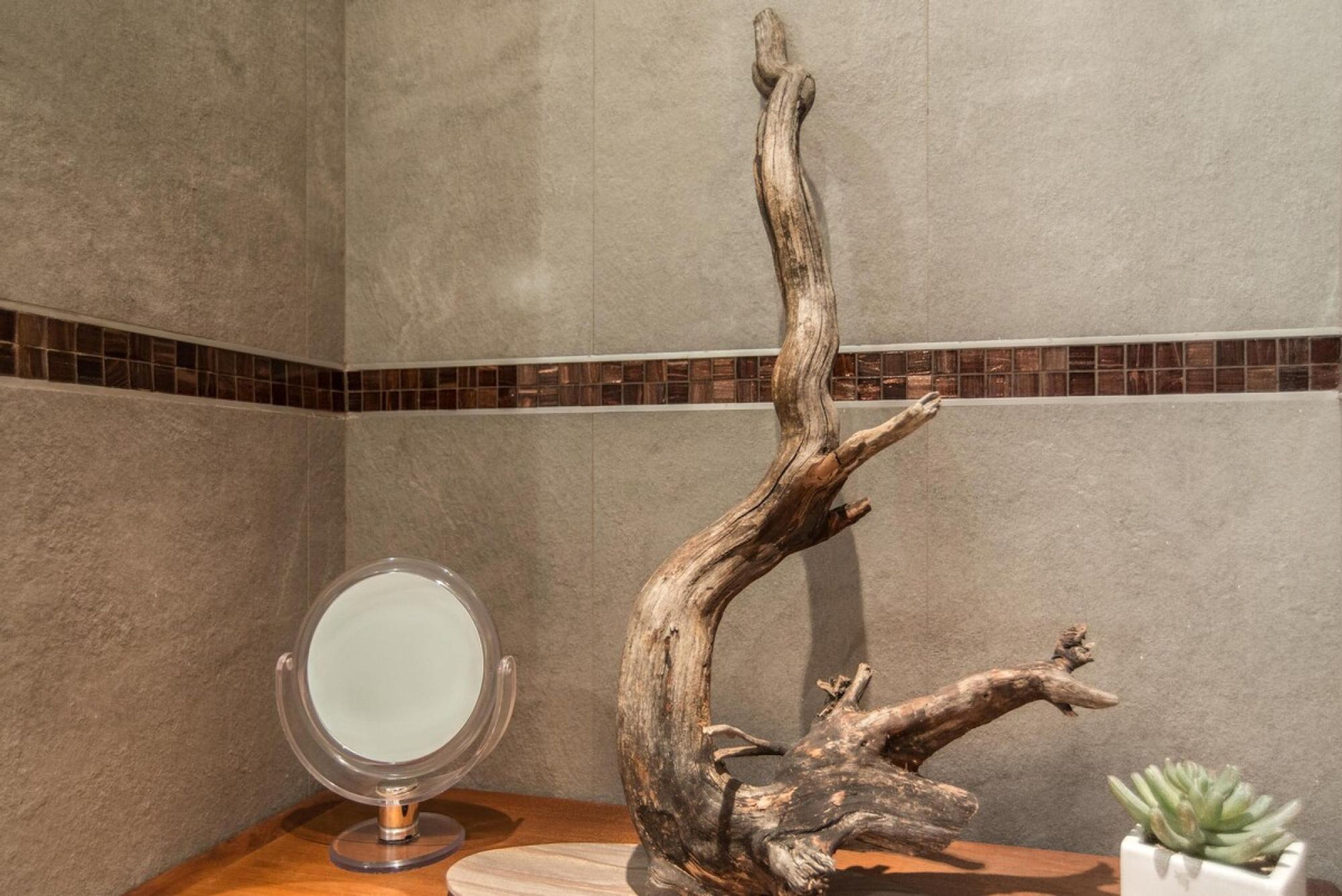 A bathroom with a mirror, a wooden sculpture, and a potted plant.