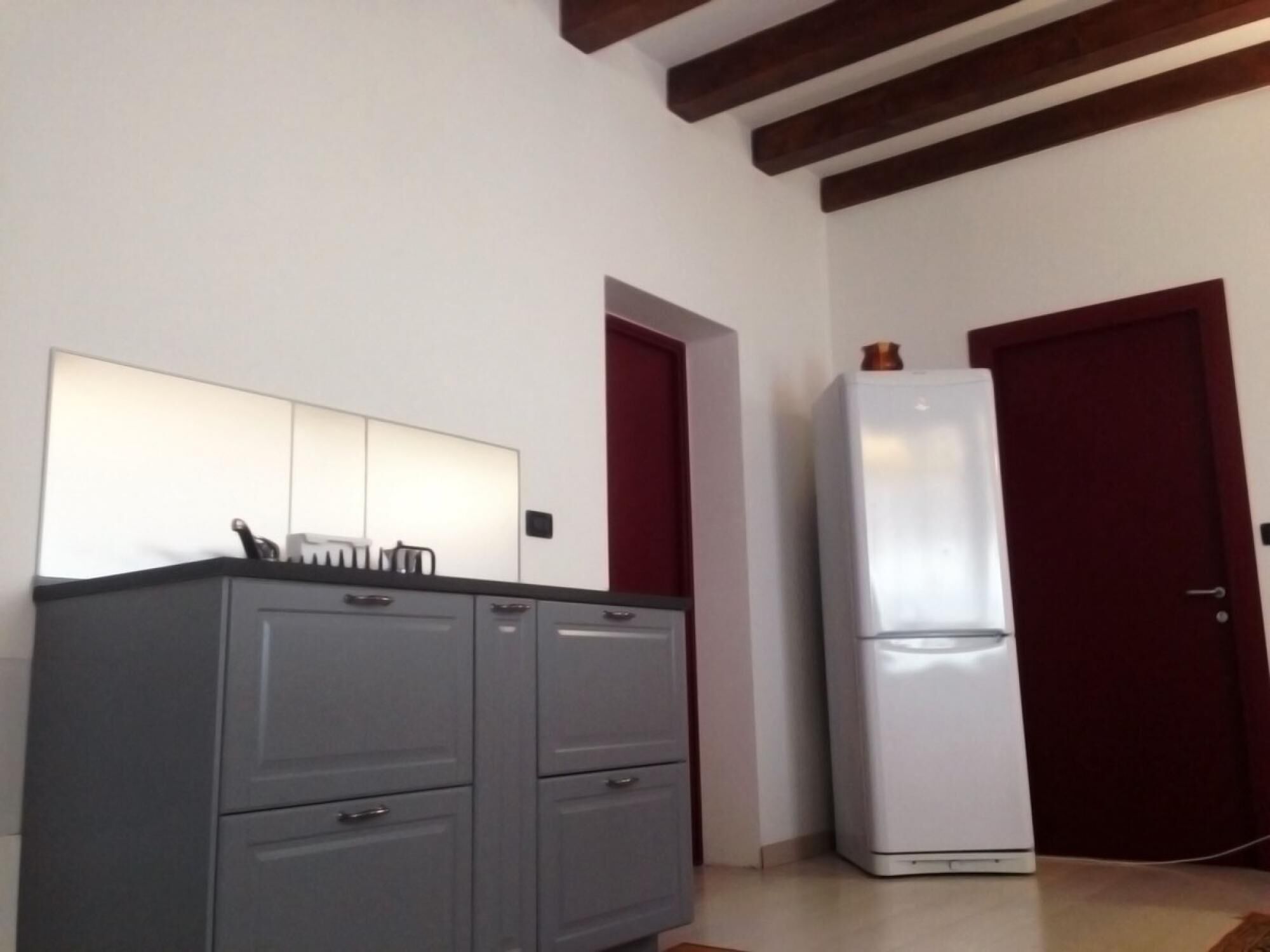 A kitchen with grey cabinets, a white refrigerator, and a red door.