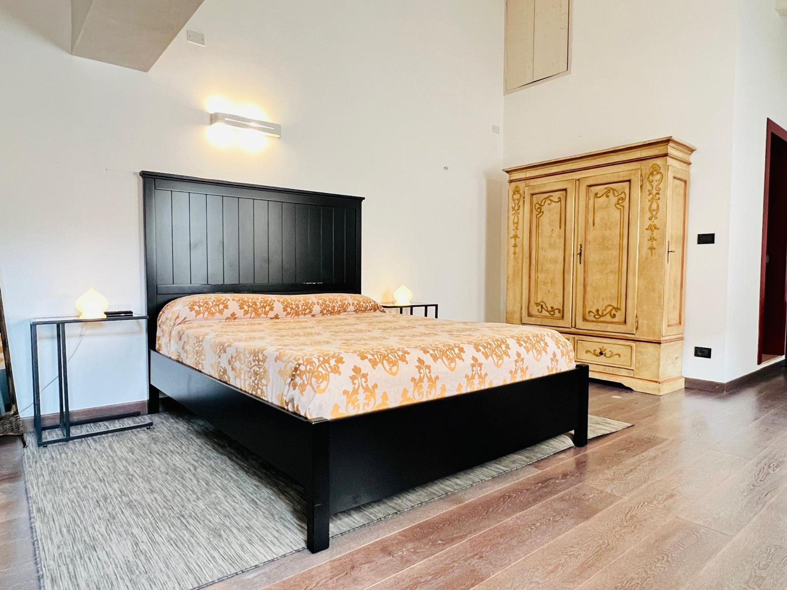 Un dormitorio con cama, mesitas de noche, armario y una lámpara en el techo.