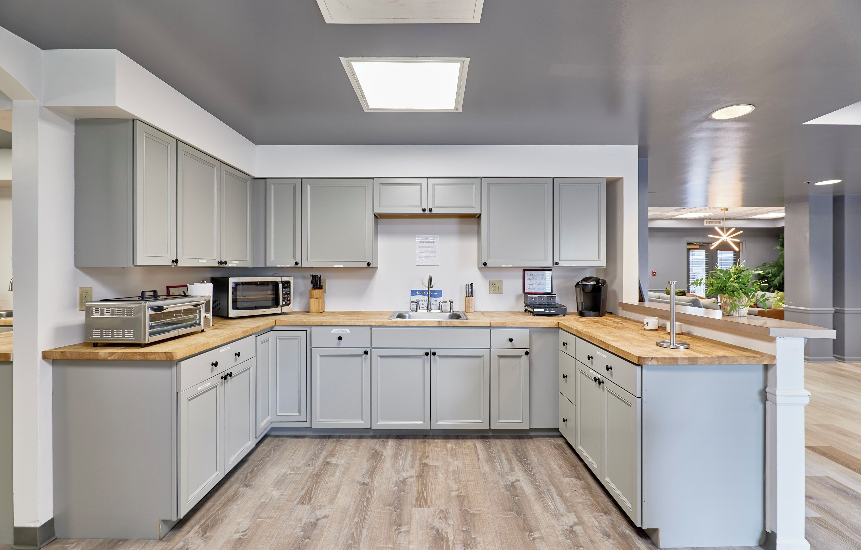 A modern kitchen with grey cabinets, a wooden countertop, and a built-in microwave.