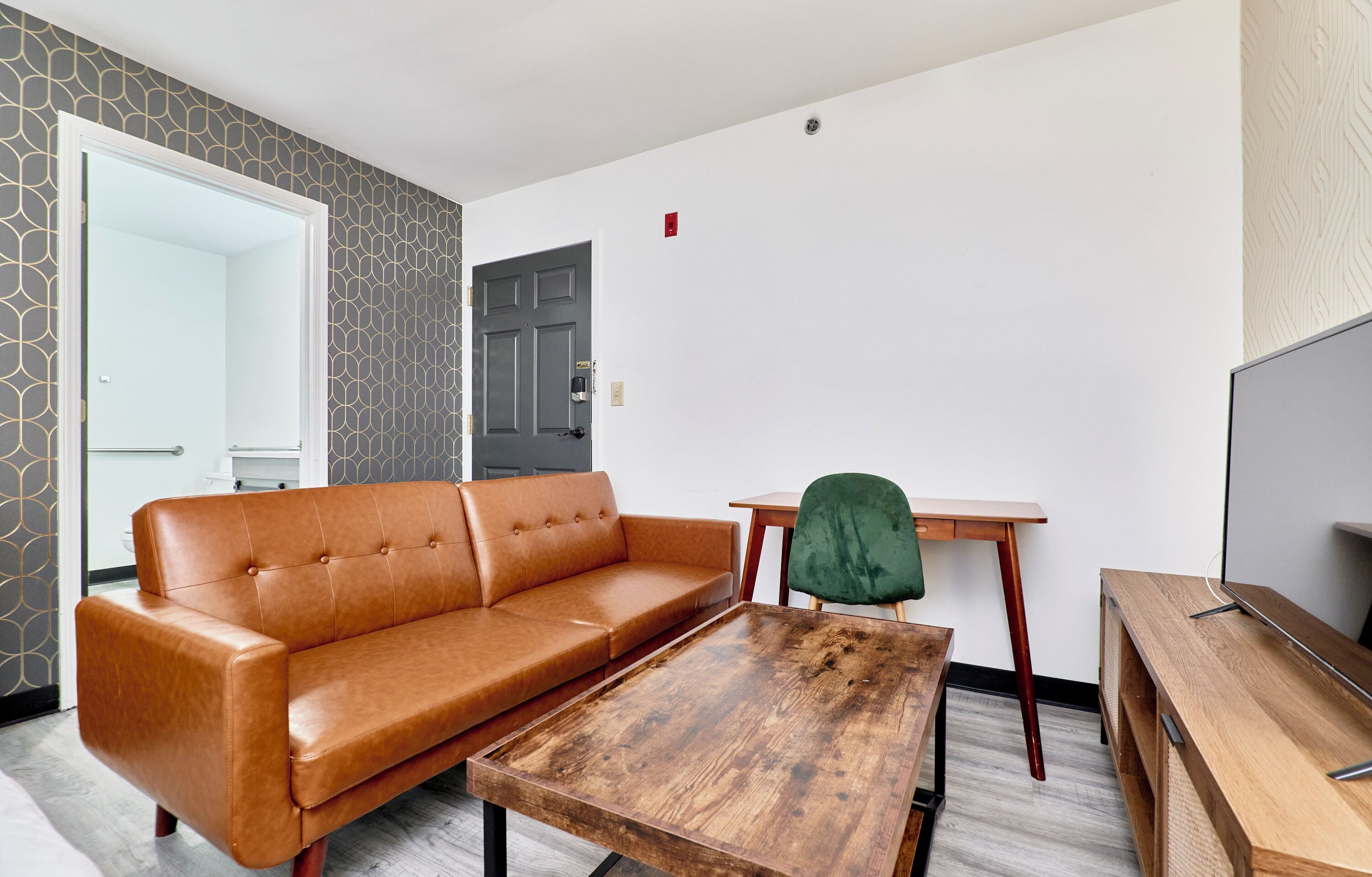 Een moderne woonkamer met een leren bank, een houten salontafel, een groene fauteuil en een televisie op een houten dressoir.
