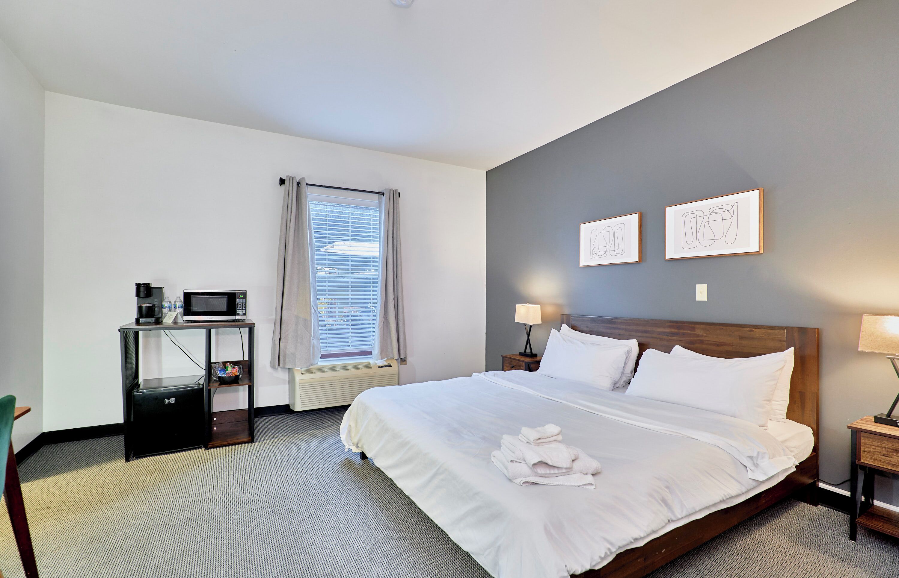 Een hotelkamer met een groot bed, een nachtkastje met een lamp, een klein bureau met een magnetron en een raam met zonwering.