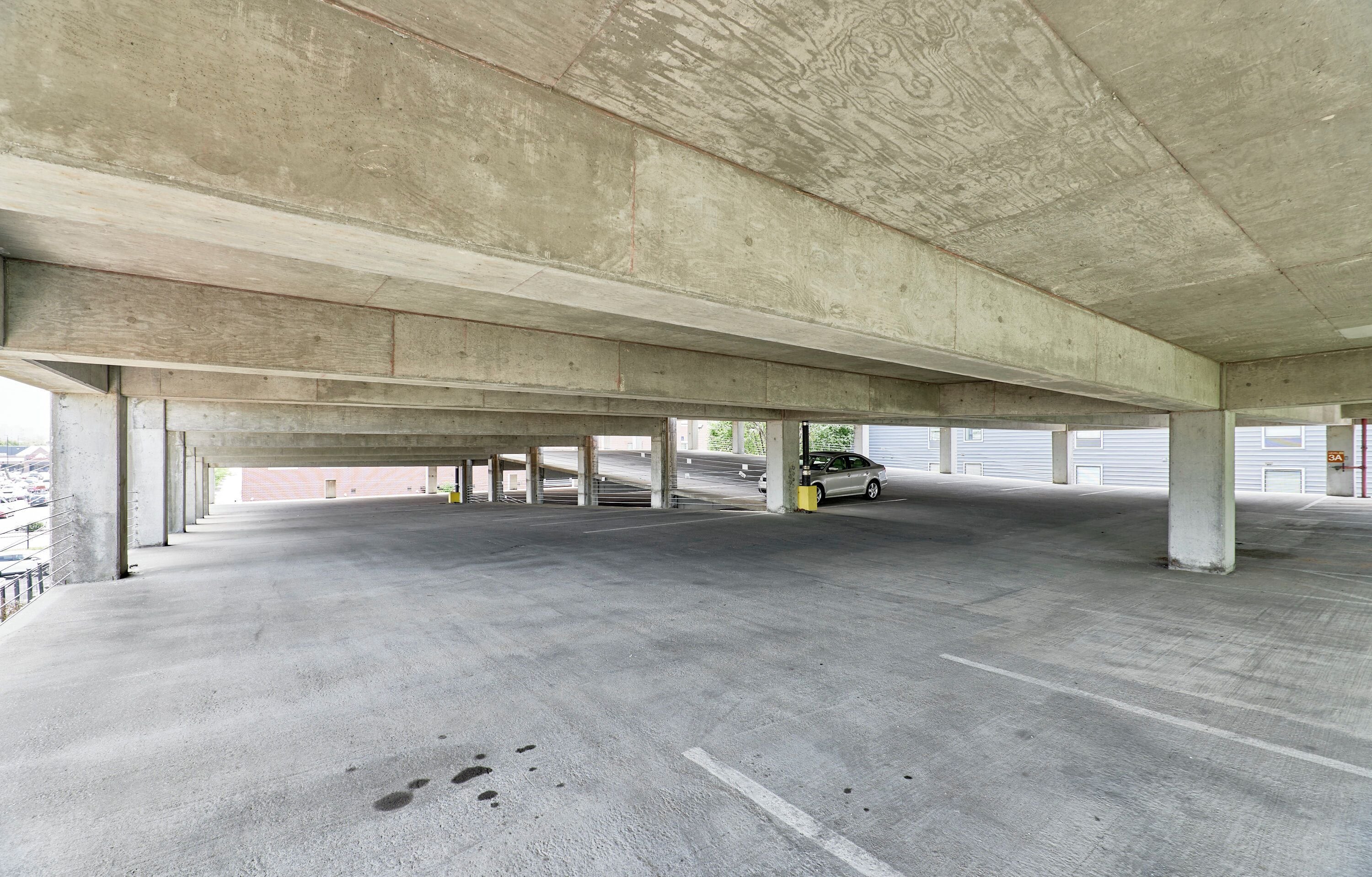An empty parking garage with concrete pillars and a grey floor.