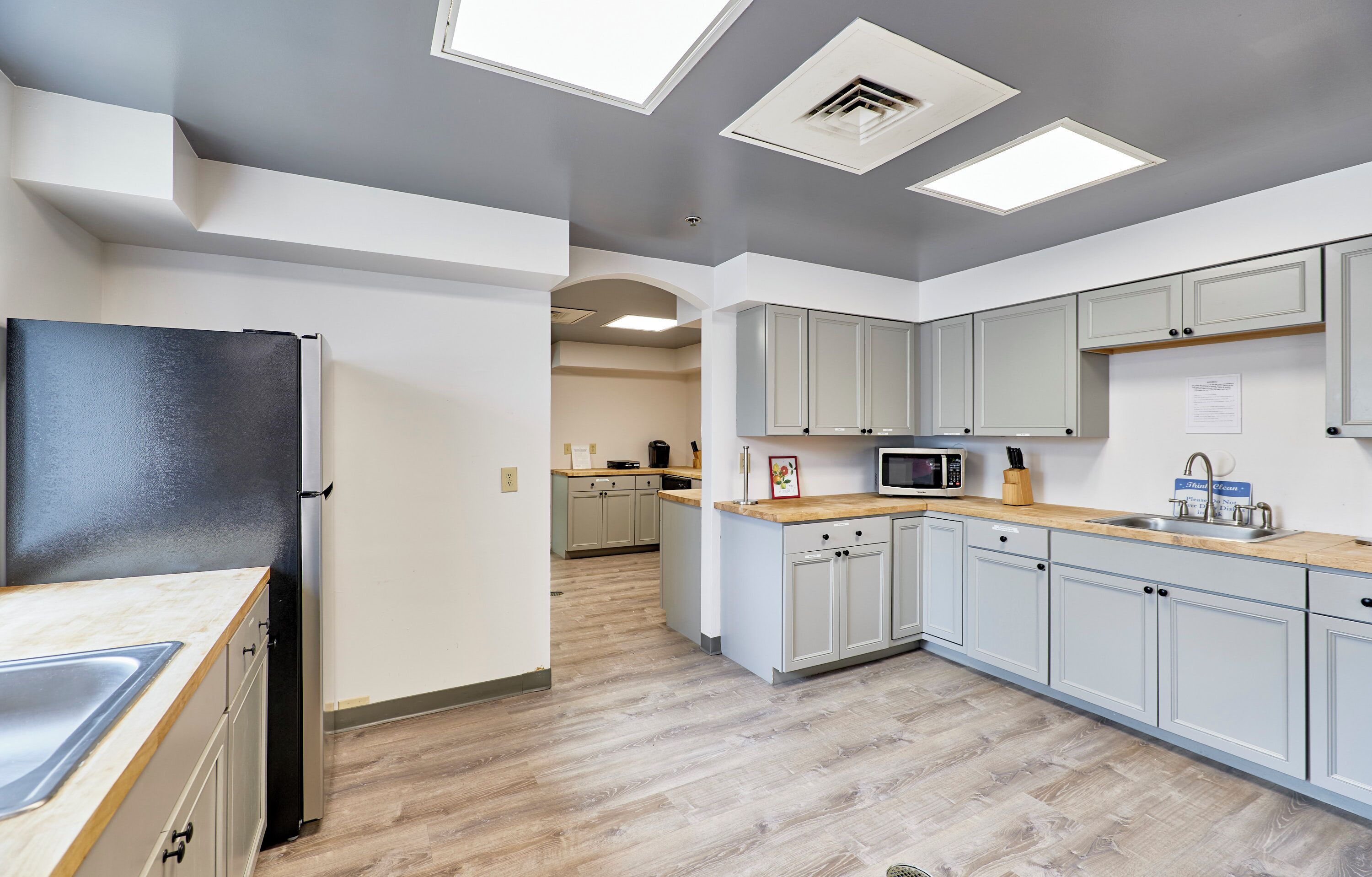 A modern kitchen with light grey cabinets, a black refrigerator, and a wooden countertop.