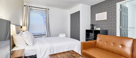 Quarto de hotel com cama, mesa de centro de madeira, sofá de couro, televisão e guarda-roupa.