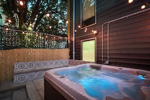 A hot tub with a wooden deck, surrounded by a bamboo fence, and string lights. - The West End (St. Louis)