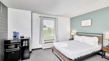 A hotel room with a bed, a desk with a microwave, a coffee maker, and a window with blinds.