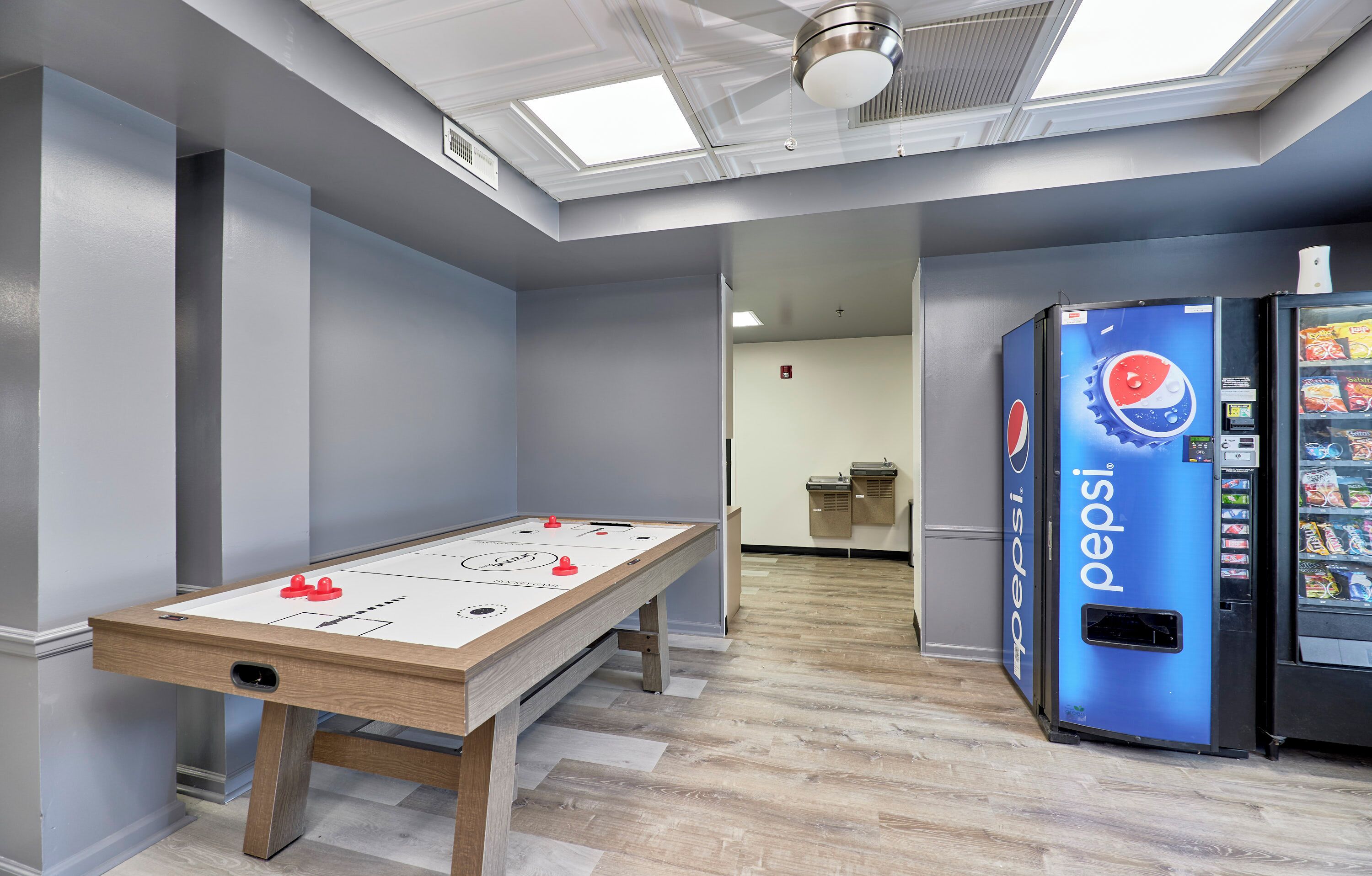 A room with a foosball table, a Pepsi vending machine, and a refrigerator.
