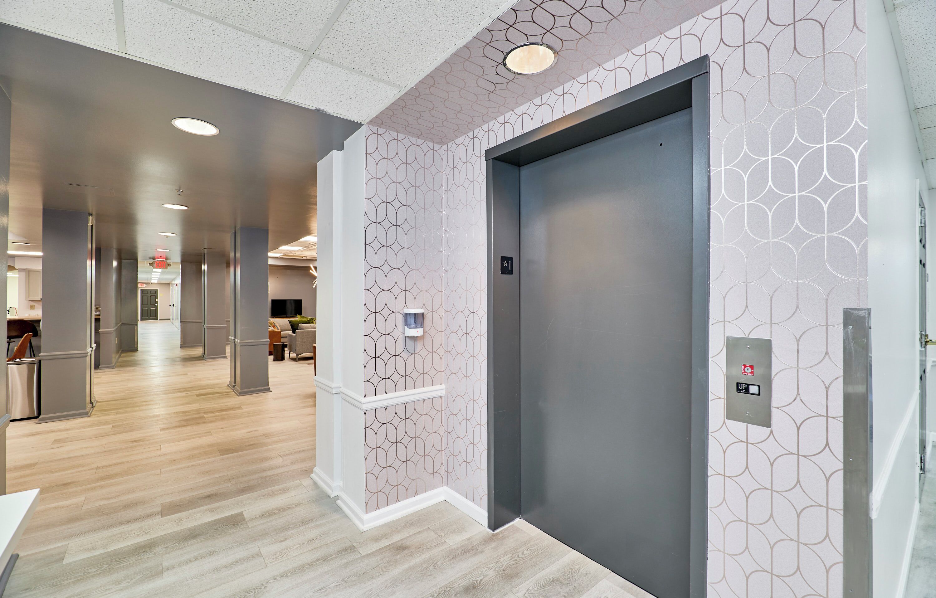 A modern elevator with a geometric wall pattern, a visible emergency phone, and a clean, well-lit interior.