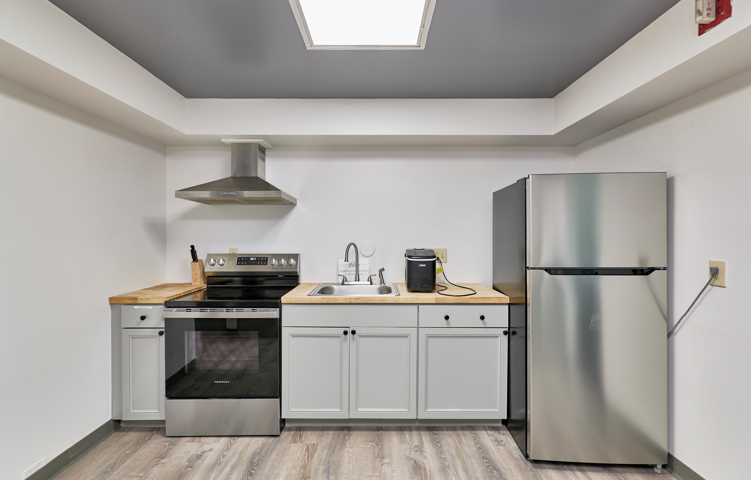 A modern kitchen with a built-in oven, a stainless steel refrigerator, and a skylight above the countertop.