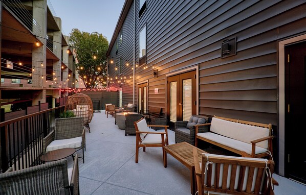 An outdoor patio with wicker furniture, a fire pit, and string lights. - The West End (St. Louis)