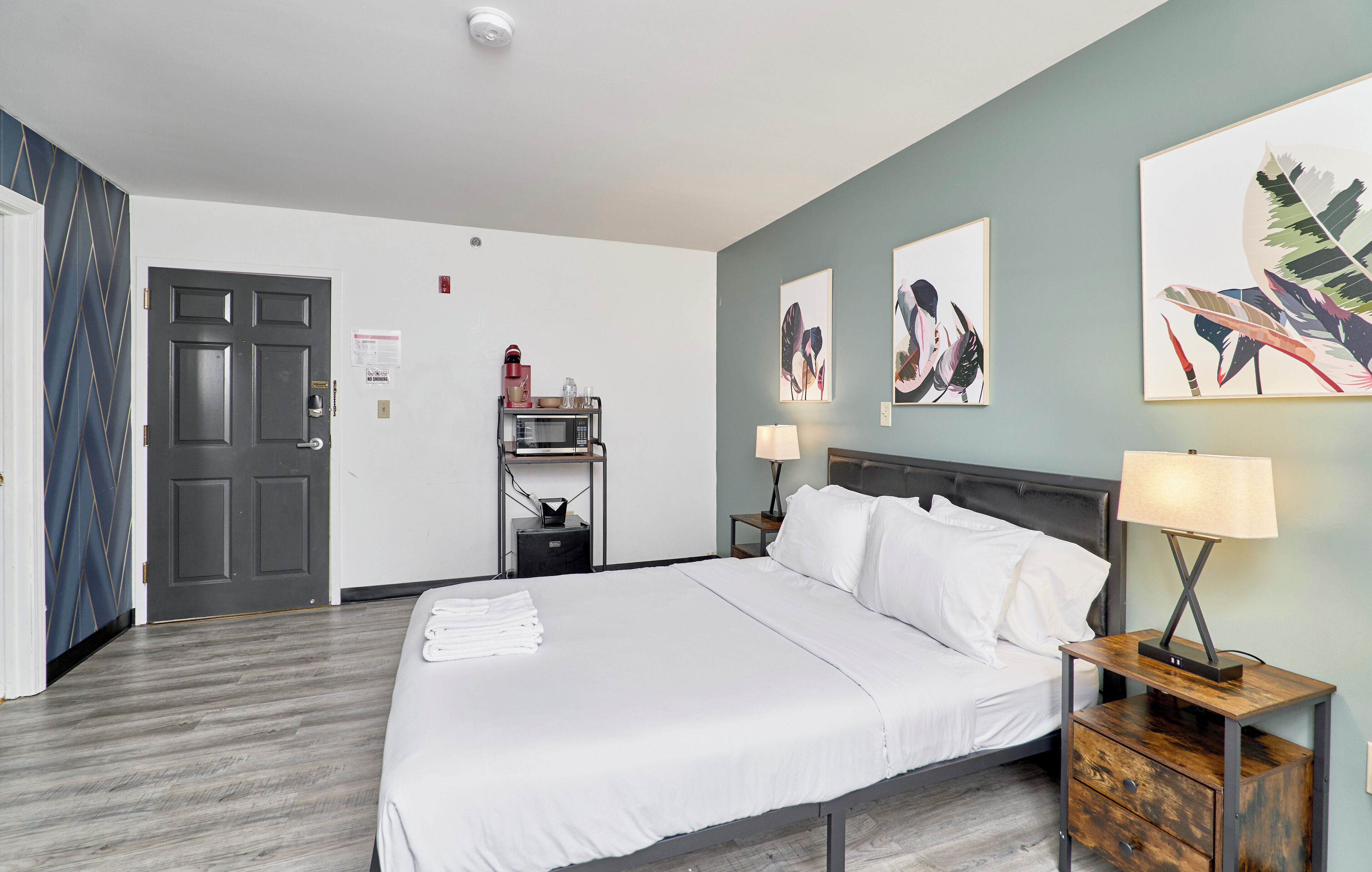 Een hotelkamer met een groot bed, twee nachtkastjes met lampen, een klein plankje met een waterkoker en kunstwerken aan de muur.