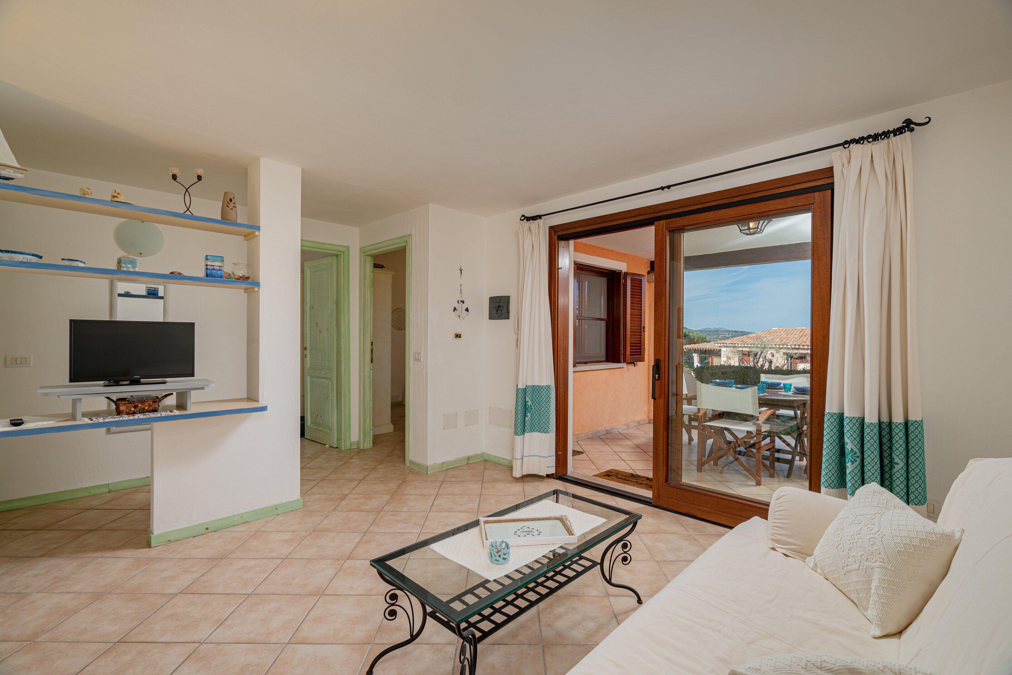 Un salón con sofá, una mesa de centro de vidrio, un televisor sobre un mueble bajo y un balcón con vistas.