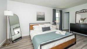 A modern bedroom with a bed, bedside tables, a floor lamp, a mirror, and a painting on the wall. - StayBurgundy Fairfield, OH (Fairfield)