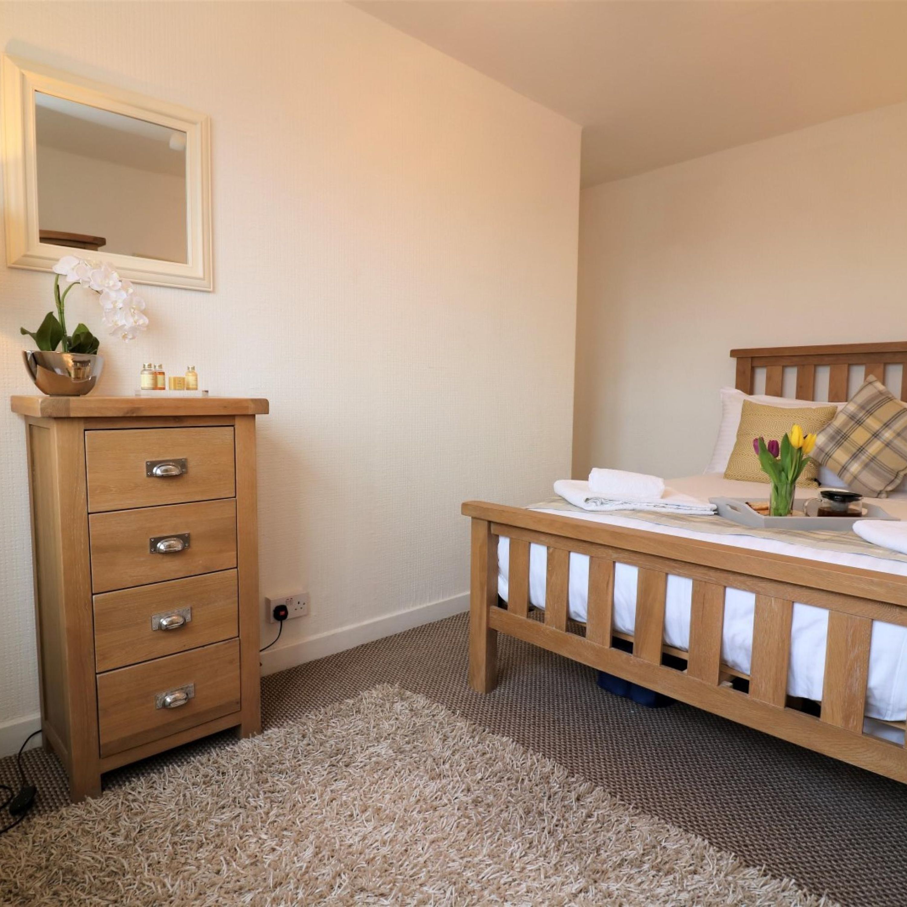 A bedroom with a wooden bed, a wooden dresser with drawers, a mirror, and a small potted orchid.