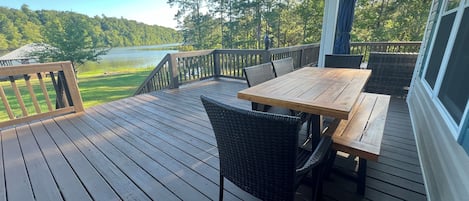 A wooden deck with a table and chairs, overlooking a lake and forest.