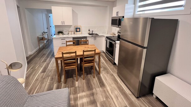 A modern kitchen with a wooden dining table, stainless steel appliances, and white cabinetry. - Brand new 2 bedroom basement in Leduc(10mins from YEG airport) (Leduc)