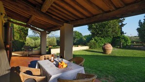 Une terrasse extérieure aménagée avec des meubles en osier, une table où sont disposés une bouteille, des verres à vin et un panier de fruits.