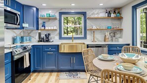 A modern kitchen with blue cabinets, a stainless steel oven, a microwave, and a window with a view of greenery. - Charming /Lake/Kayak/Firepit/Hot tub/Pets (Blakeslee)