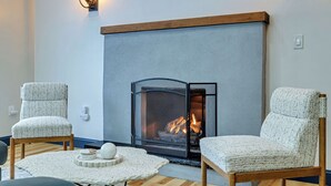 A cozy room with a fireplace, two upholstered chairs, a small round table with a decorative object, and wall-mounted lighting. - Charming /Lake/Kayak/Firepit/Hot tub/Pets (Blakeslee)